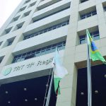 Prédio da Justiça do Trabalho com a bandeira do Brasil e outras bandeiras, em frente a um céu azul claro.