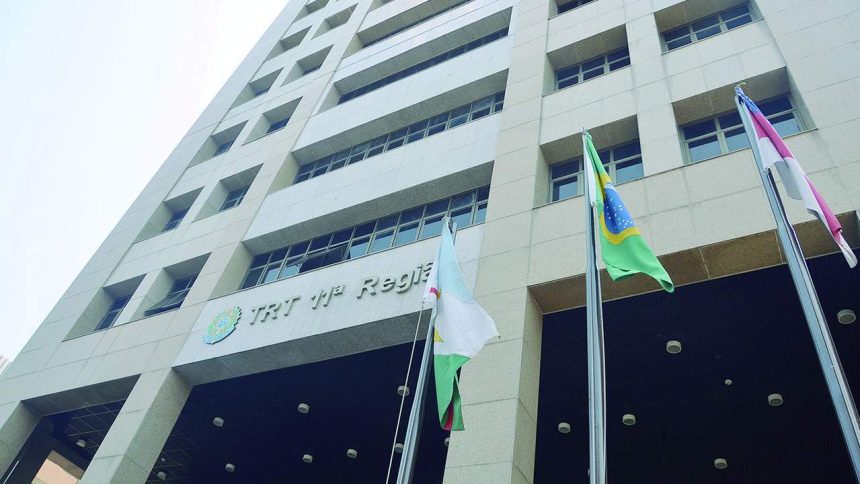 Prédio da Justiça do Trabalho com a bandeira do Brasil e outras bandeiras, em frente a um céu azul claro.