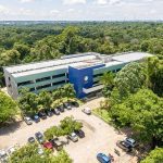 Prédio moderno em um campus universitário, cercado por árvores e com um estacionamento na frente.