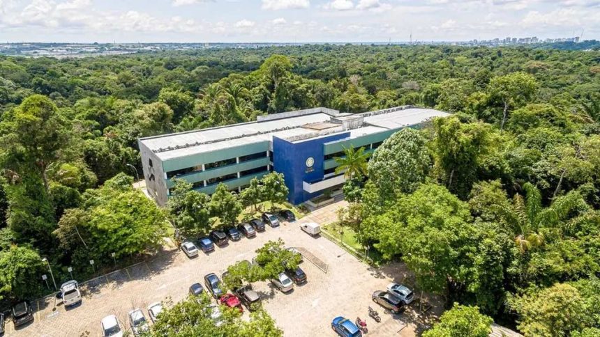 Prédio moderno em um campus universitário, cercado por árvores e com um estacionamento na frente.