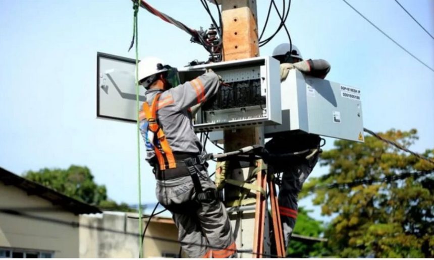 Técnicos trabalhando em um poste de energia com equipamentos de segurança, realizando manutenção na rede elétrica.