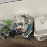 Três sacolas plásticas cheias de aparelhos eletrônicos e caixas, provavelmente para descarte ou reciclagem.