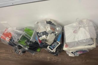 Três sacolas plásticas cheias de aparelhos eletrônicos e caixas, provavelmente para descarte ou reciclagem.