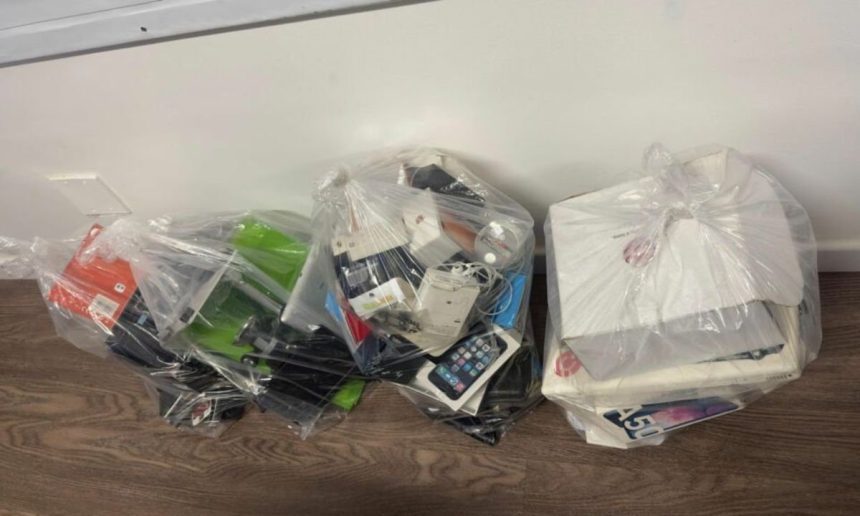 Três sacolas plásticas cheias de aparelhos eletrônicos e caixas, provavelmente para descarte ou reciclagem.