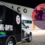 Um caminhão preto da IML-DPTC com a inscrição "Amazonas" estacionado em frente a um prédio, com uma cena de crime sendo investigada por policiais em segundo plano.