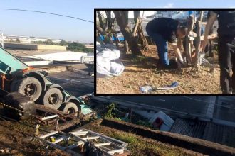 Um caminhão tombado em um acidente com um homem ao fundo no local do acidente