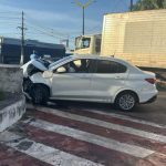 Um carro branco, aparentemente acidentado, encontra-se em um cruzamento, com a frente amassada e sinais de colisão.