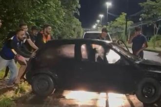 Um carro preto envolvido em um acidente, com pessoas ao redor, em uma rua à noite.
