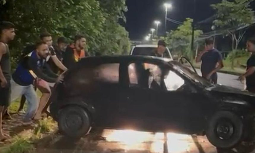 Um carro preto envolvido em um acidente, com pessoas ao redor, em uma rua à noite.