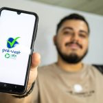 Um estudante sorridente segurando seu celular, exibindo o aplicativo do Pré-Vest, curso preparatório para o vestibular da Universidade do Estado do Amazonas (UEA).
