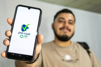 Um estudante sorridente segurando seu celular, exibindo o aplicativo do Pré-Vest, curso preparatório para o vestibular da Universidade do Estado do Amazonas (UEA).