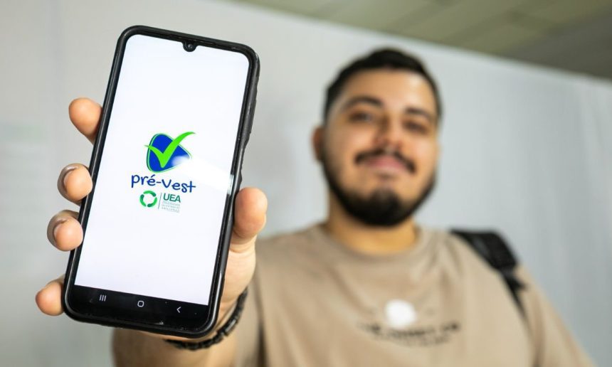 Um estudante sorridente segurando seu celular, exibindo o aplicativo do Pré-Vest, curso preparatório para o vestibular da Universidade do Estado do Amazonas (UEA).