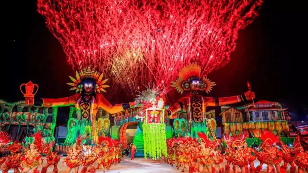 Um festival de rua com dançarinos em trajes coloridos e fogos de artifício, sob um céu noturno. A imagem captura a alegria e a energia vibrante do evento.