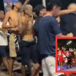 Um grupo de pessoas em uma rua à noite, algumas delas usando camisetas vermelhas. No fundo, um policial de moto. A imagem pode ser relacionada a um incidente de violência.