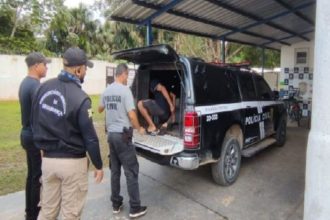 Um homem detido pela polícia, sendo levado para a viatura.