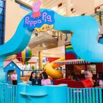 Um parque temático da Peppa Pig, com cores vibrantes, em um shopping, com uma estrutura de escalada em forma de onda e outras atividades infantis.