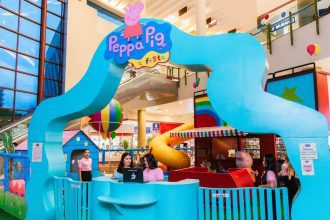 Um parque temático da Peppa Pig, com cores vibrantes, em um shopping, com uma estrutura de escalada em forma de onda e outras atividades infantis.