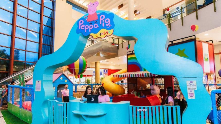 Um parque temático da Peppa Pig, com cores vibrantes, em um shopping, com uma estrutura de escalada em forma de onda e outras atividades infantis.