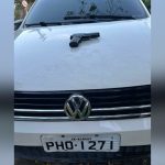 Uma arma de fogo preta sobre o capô de um carro branco com a placa PHO-1271, AM-Manaus.