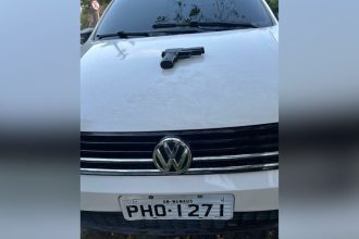 Uma arma de fogo preta sobre o capô de um carro branco com a placa PHO-1271, AM-Manaus.