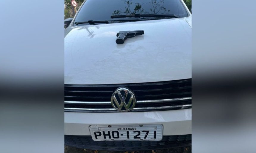 Uma arma de fogo preta sobre o capô de um carro branco com a placa PHO-1271, AM-Manaus.