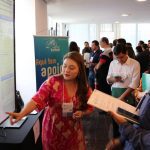 Uma mulher aponta para uma apresentação sobre oncologia em um congresso científico, enquanto um homem a escuta e segura um tablet.