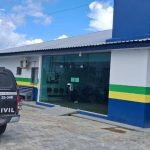 Viatura da Polícia Civil preta e branca parada em frente a uma delegacia, com um homem sendo preso.