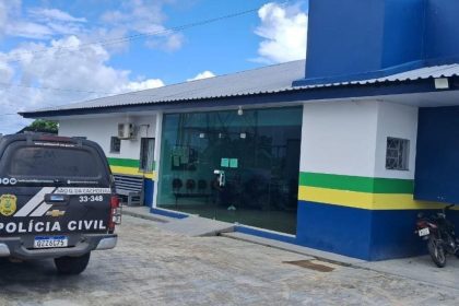 Viatura da Polícia Civil preta e branca parada em frente a uma delegacia, com um homem sendo preso.