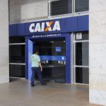 Imagem colorida mostra trabalhador entrando em agência da Caixa Econômica