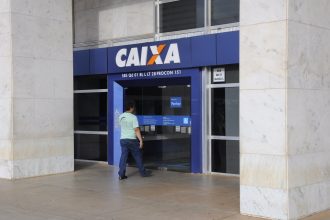 Imagem colorida mostra trabalhador entrando em agência da Caixa Econômica