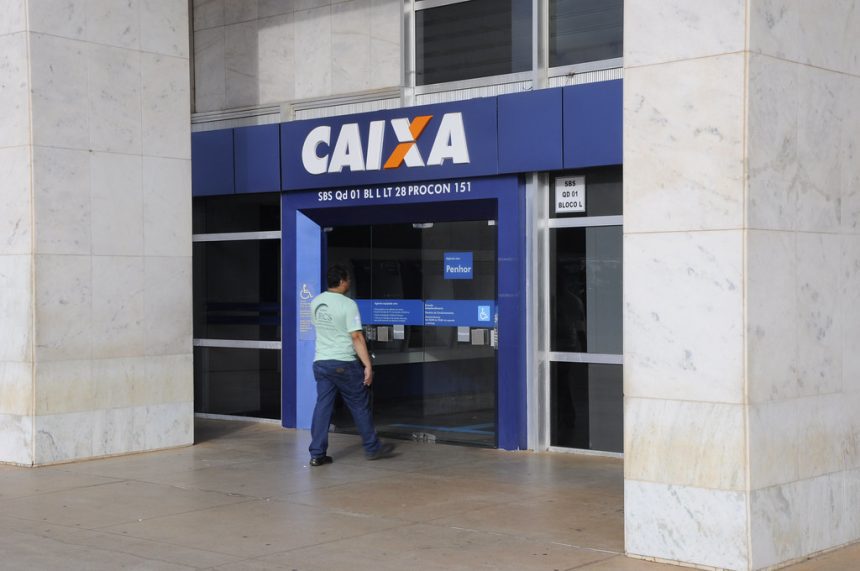 Imagem colorida mostra trabalhador entrando em agência da Caixa Econômica