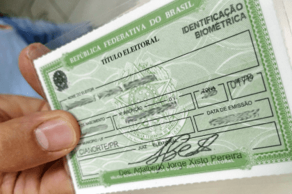 Imagem colorida mostra título de eleitor na mão de uma pessoa