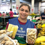 Imagem colorida mostra Feirante oferecendo seus produtos na Feira da ADS