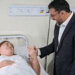 Imagem colorida mostra o governador Wilson Lima conversando com uma paciente no hospital Adriano Jorge