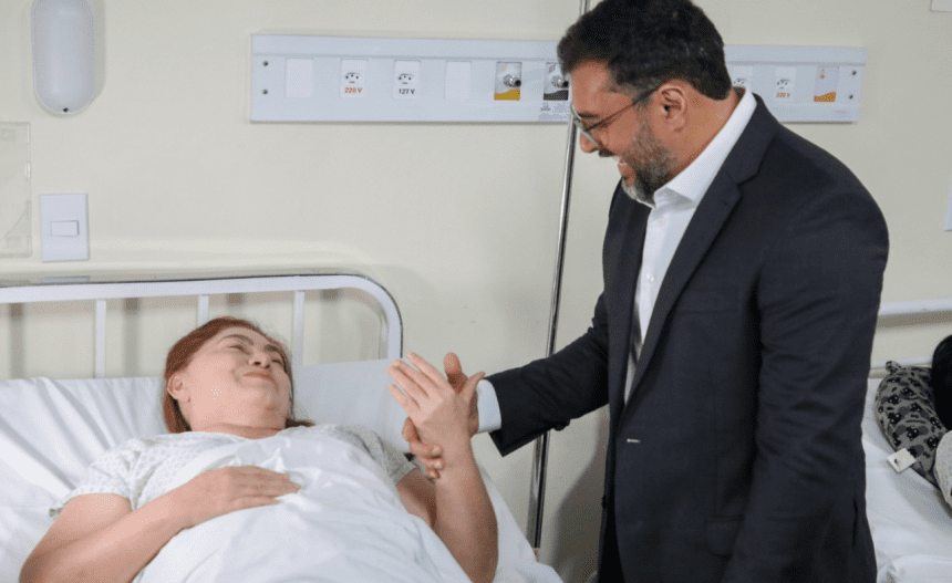 Imagem colorida mostra o governador Wilson Lima conversando com uma paciente no hospital Adriano Jorge