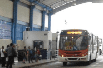 Imagem colorida mostra ônibus e passageiros esperando para pagamento em dinheiro