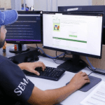 Imagem colorida mostra Pessoa em frente a um computador mostrando aceso ao site do Bolsa Universidade Manaus