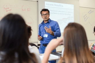 Imagem colorida mostra professor dando aula em sala com estudantes atentos para falar sobre Prova Nacional para Contratação de Professores