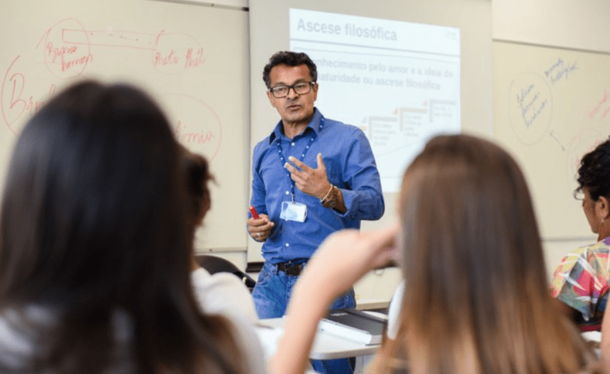 Imagem colorida mostra professor dando aula em sala com estudantes atentos para falar sobre Prova Nacional para Contratação de Professores