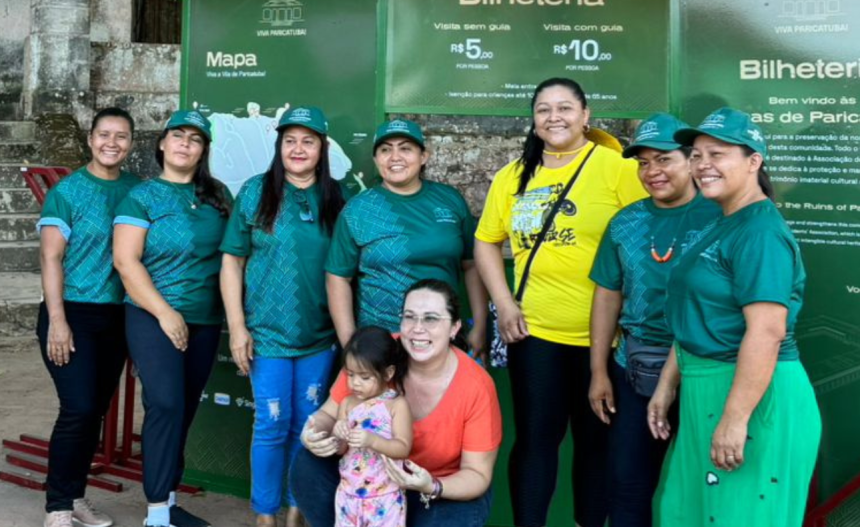 Imagem colorida mostra comunitários da Vila de Paricatuba em frente a banner do Projeto Viva Paricatuba
