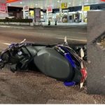 Acidente com moto em avenida de Manaus após buraco, com buraco na pista e posto de gasolina ao fundo.
