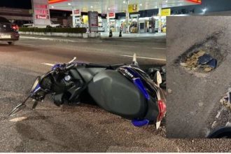Acidente com moto em avenida de Manaus após buraco, com buraco na pista e posto de gasolina ao fundo.