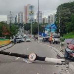 Acidente de carro em via urbana, com veículo danificado e poste caído.