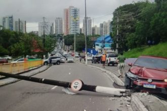 Acidente de carro em via urbana, com veículo danificado e poste caído.