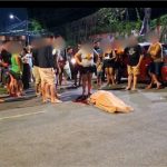 Acidente de trânsito com vítima fatal em avenida, com pessoas ao redor e carro vermelho.