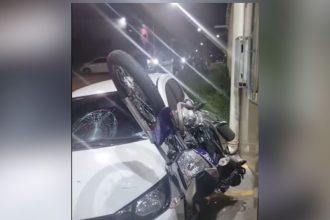 Acidente de trânsito: motocicleta colide com carro, vidro quebrado e moto em cima.