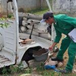 Agente de saúde inspecionando um veículo abandonado em busca de focos de dengue.