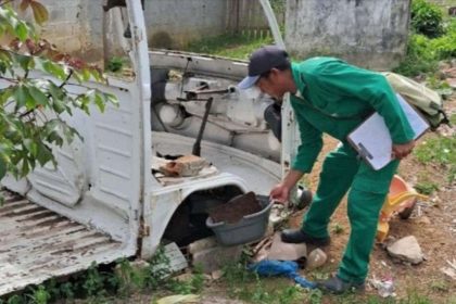 Agente de saúde inspecionando um veículo abandonado em busca de focos de dengue.