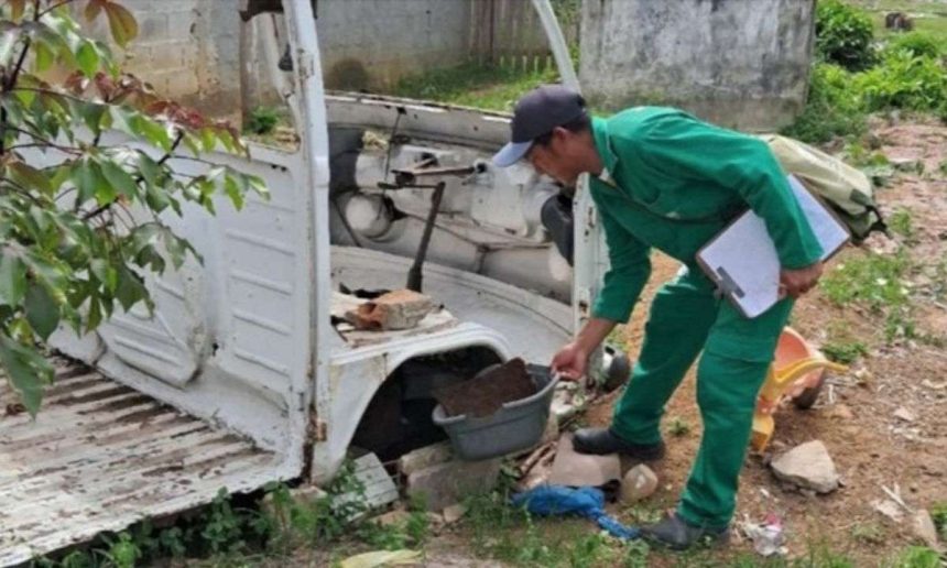 Agente de saúde inspecionando um veículo abandonado em busca de focos de dengue.