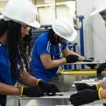 Alunos do SENAI em treinamento com capacetes e óculos de proteção em um laboratório.